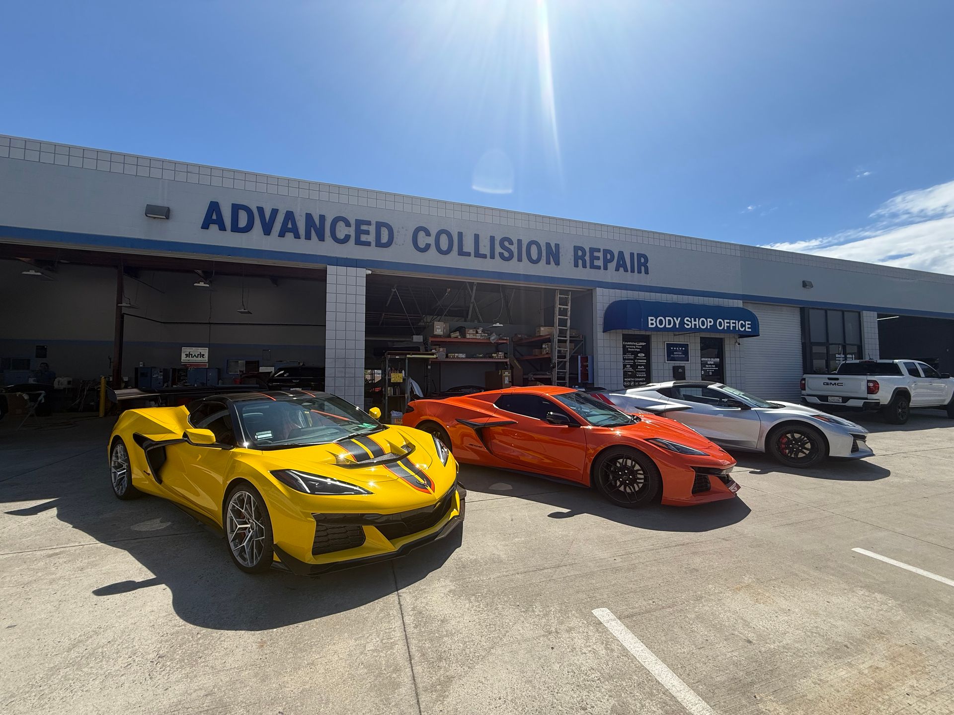 Yellow, orange, and silver sports cars parked outside Advanced Collision Repair shop
