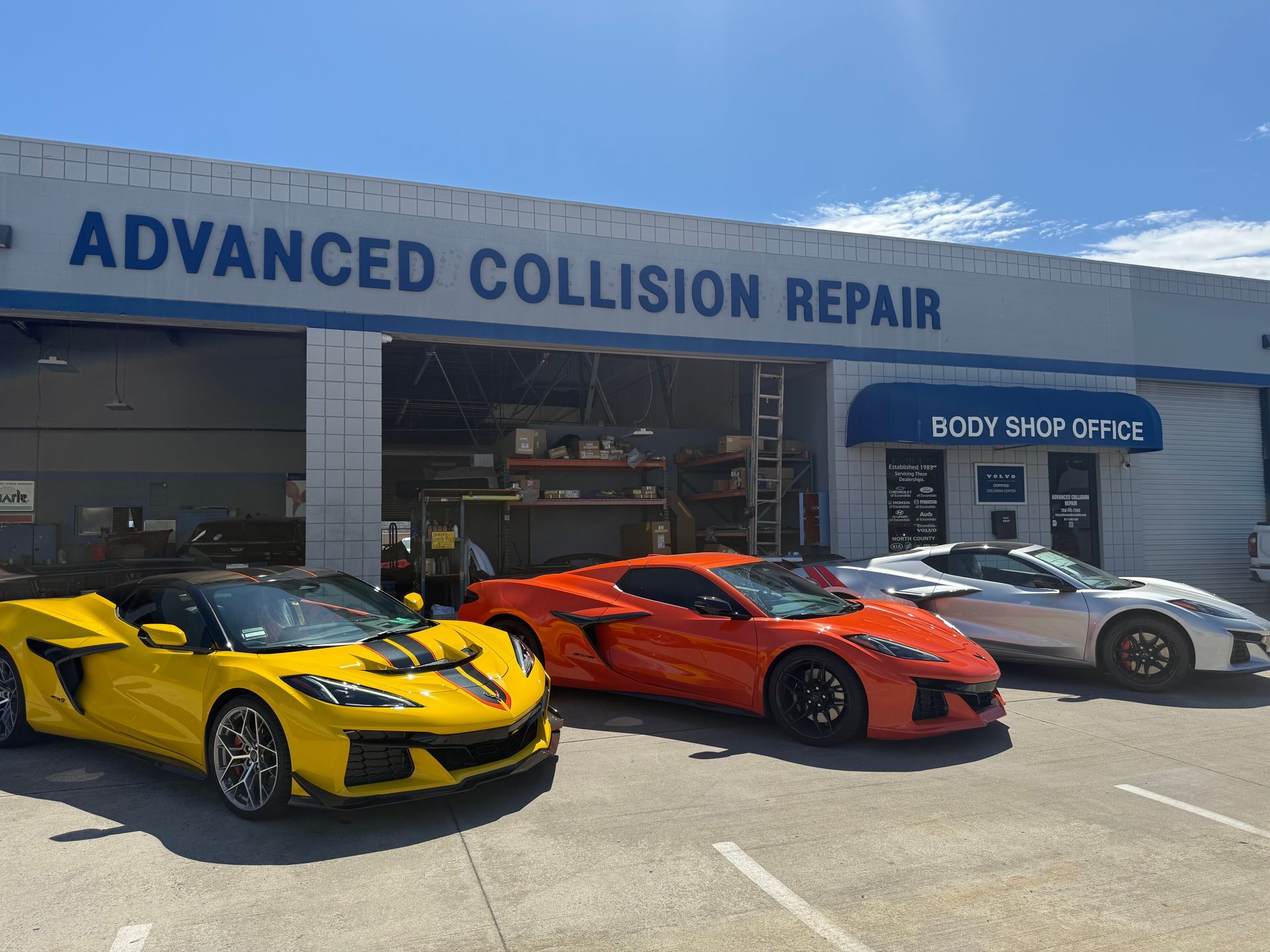Three sports cars parked outside an advanced collision repair shop on a sunny day.