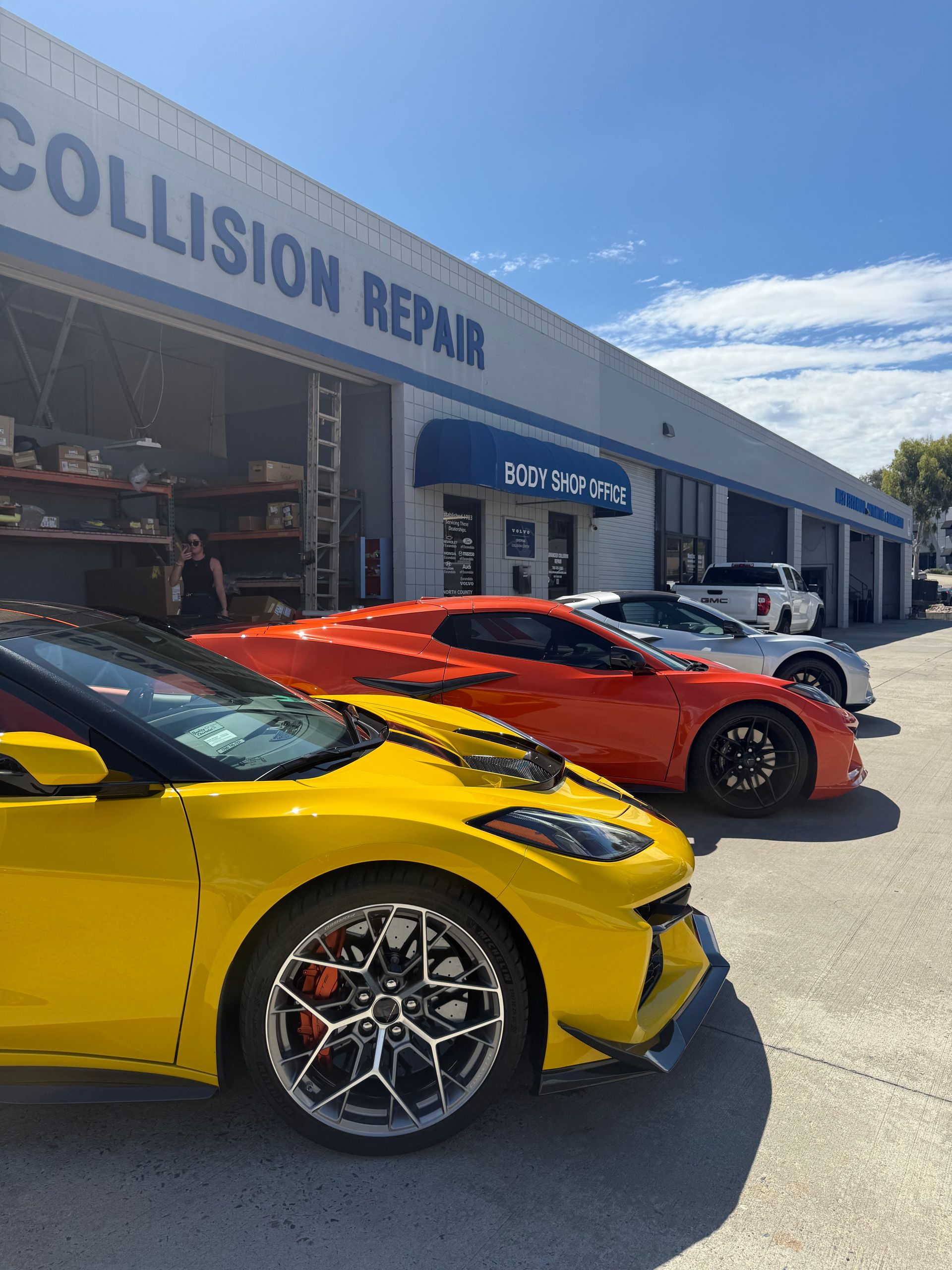 Two sports cars parked outside a collision repair shop on a sunny day