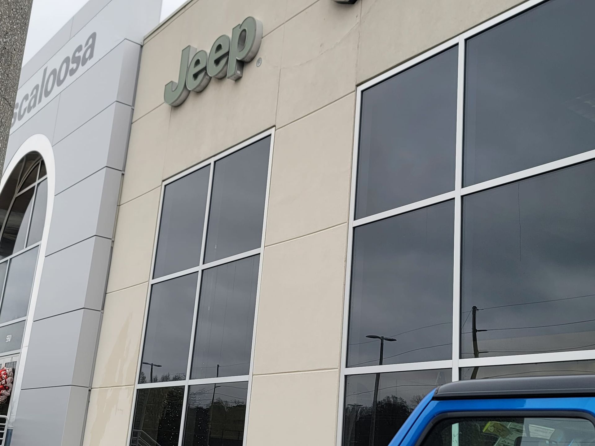 A blue jeep is parked in front of a jeep dealership