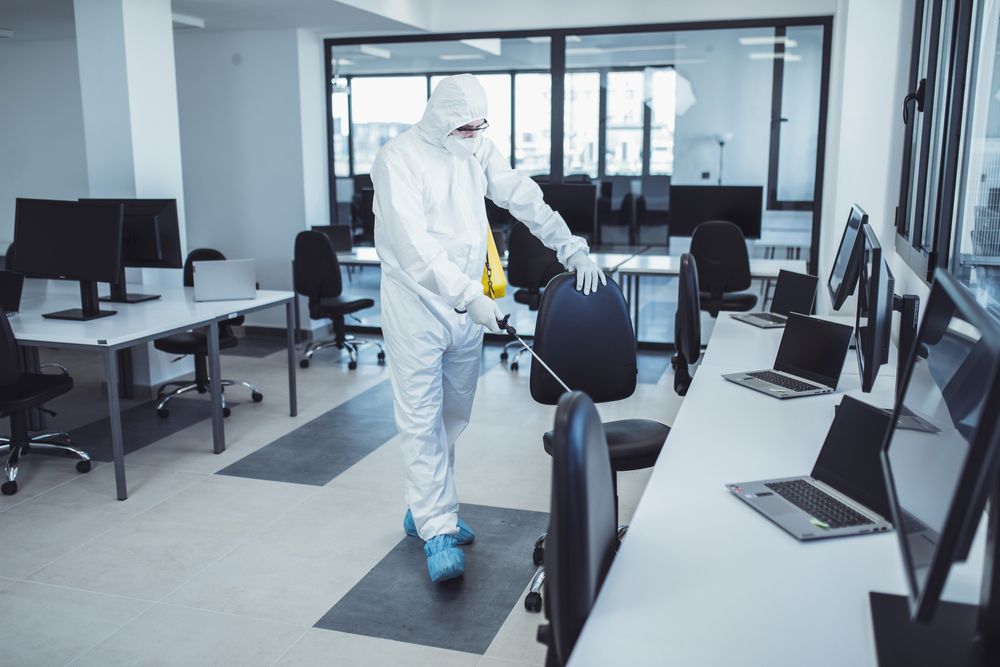 A man in a protective suit is disinfecting an office.