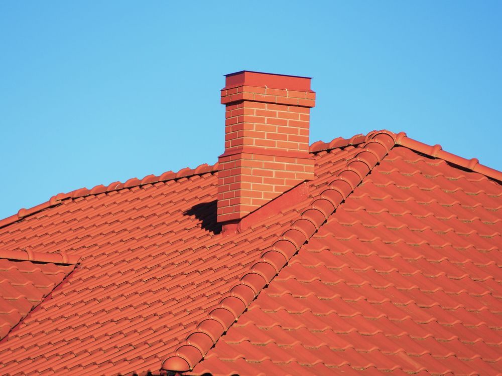 A brick chimney on top of a red tiled roof.