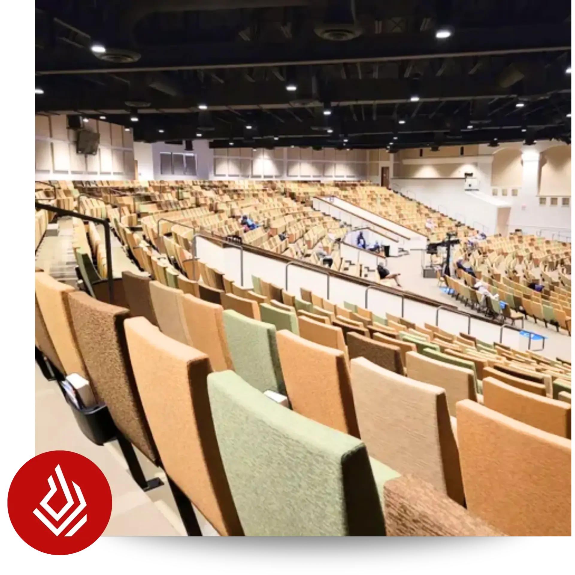 A large, empty auditorium viewed from the upper level, showing curved rows of tan, brown, and green seats.