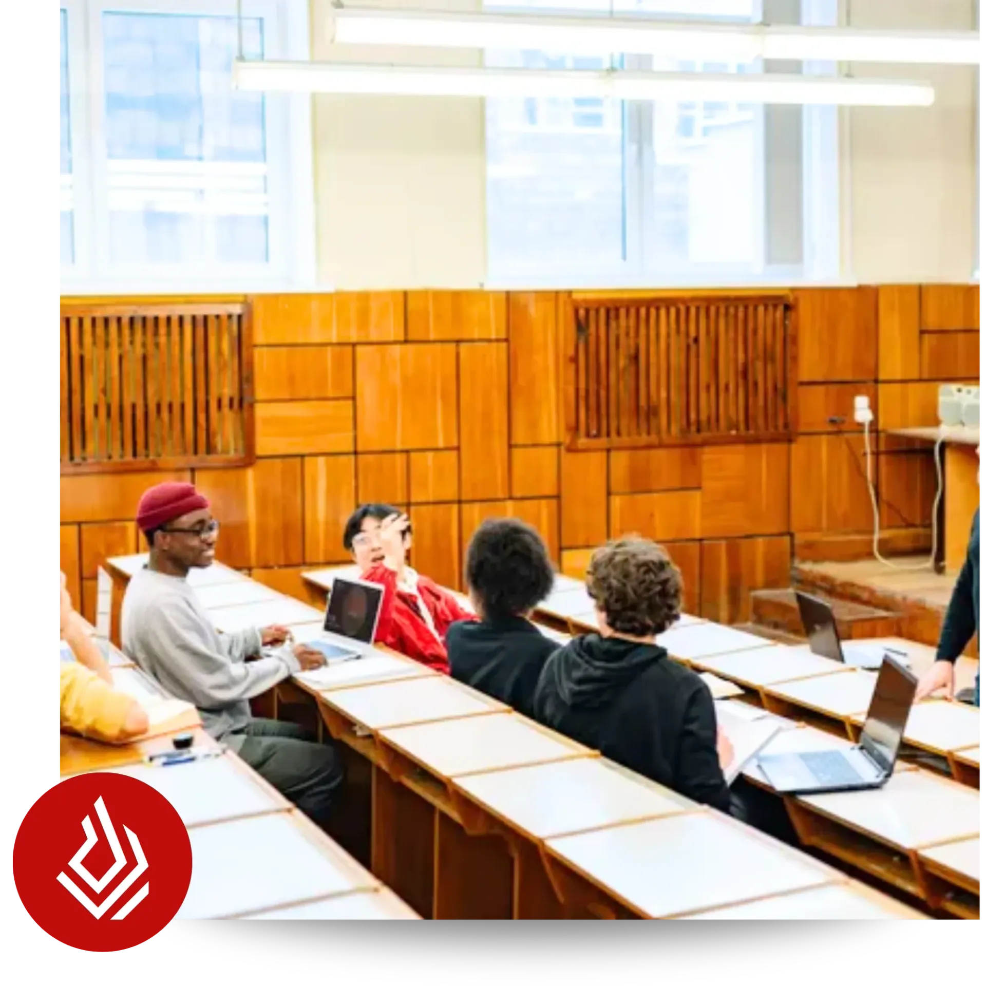 Students sitting at tiered desks using laptops in a wood-paneled lecture hall