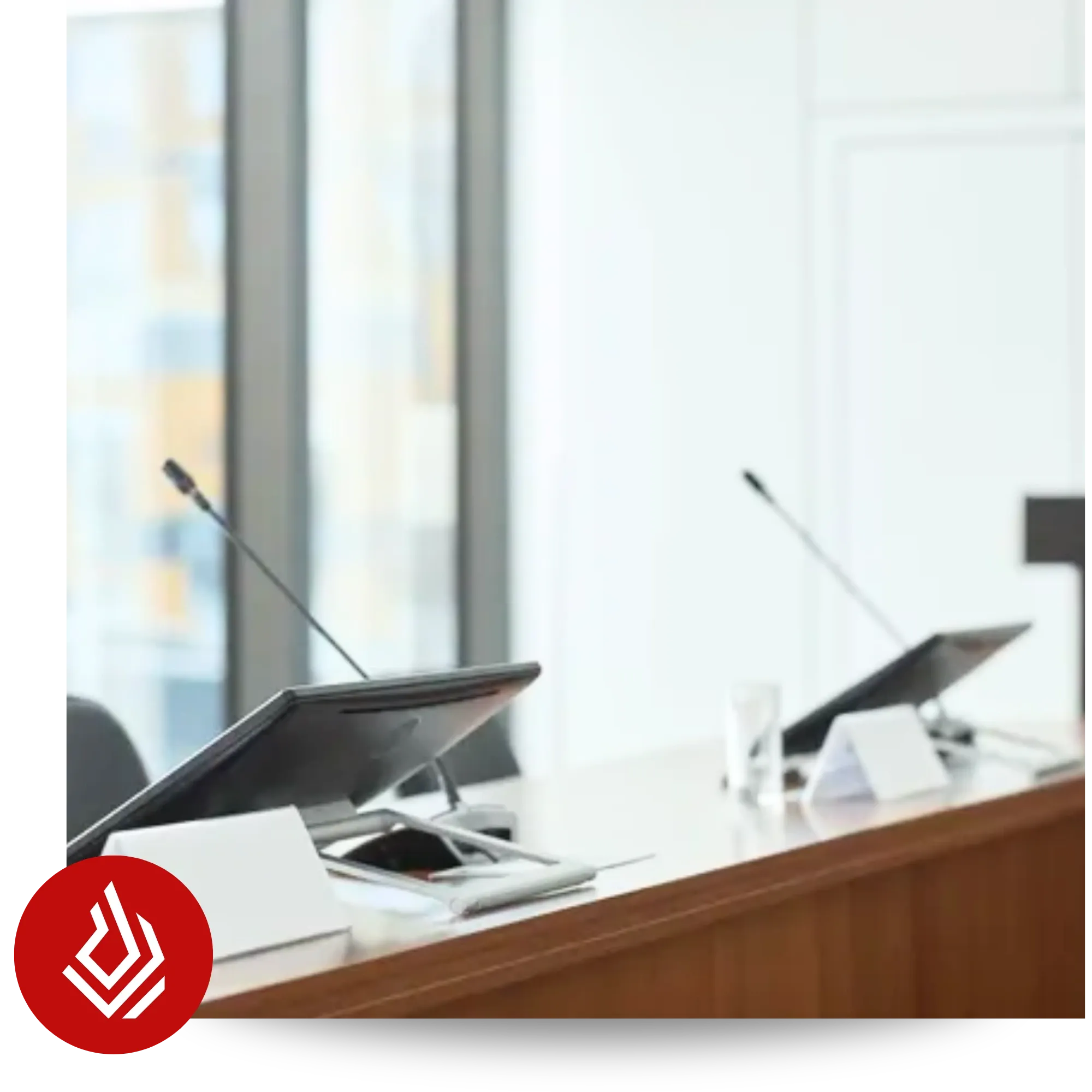 An empty wooden desk equipped with microphones and digital screens in a bright, modern hearing or conference room
