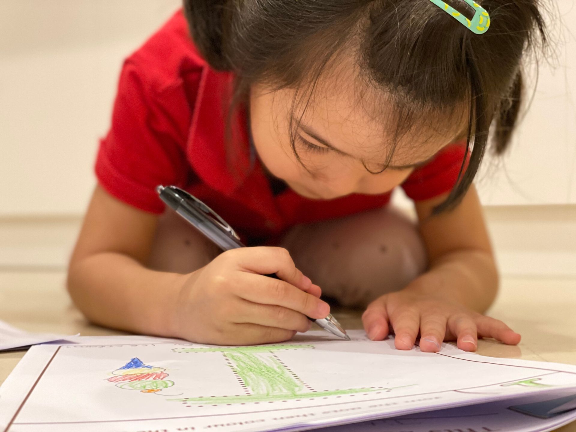 A little girl is writing on a piece of paper with a pen.