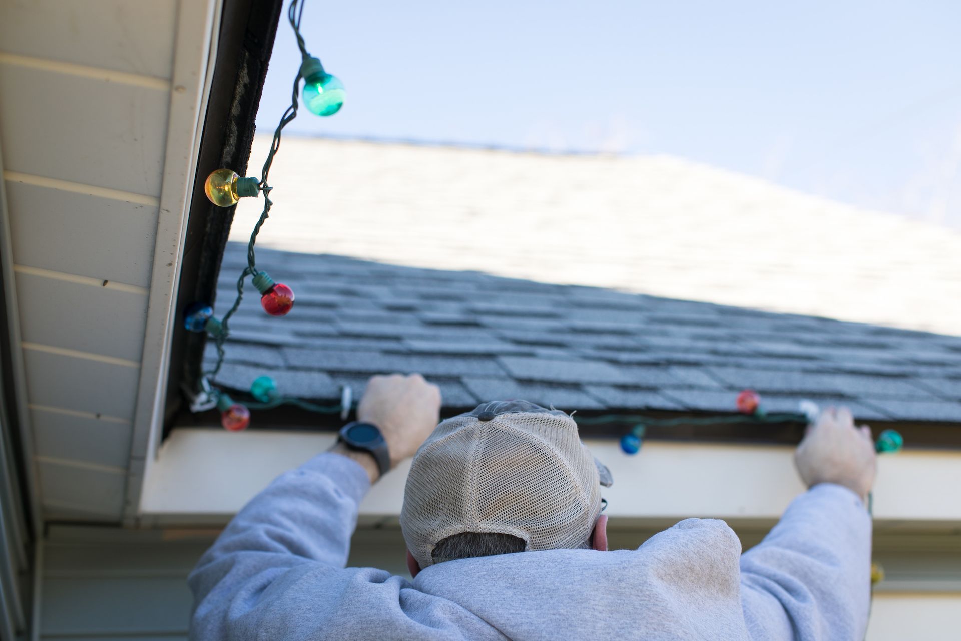Person hanging colorful Christmas lights on a house's roof.