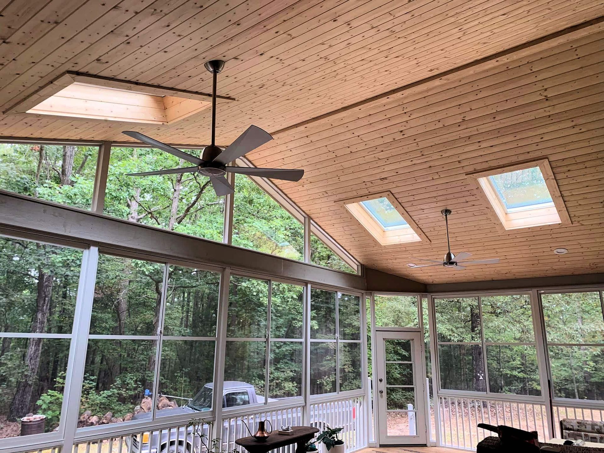 Screened porch with wood ceiling, ceiling fan, skylights, and a forest view through large windows
