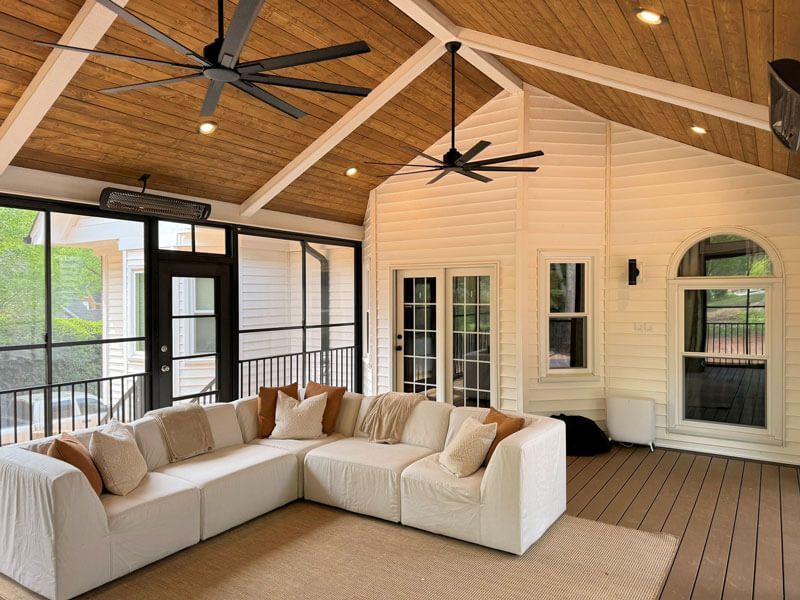 Modern covered porch with white sectional sofa, wood ceiling, ceiling fans, and screened windows