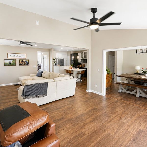 Bright open living room with beige sectional, wood floors, ceiling fan, and dining area visible through doorway