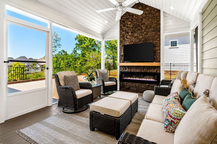 Bright covered patio with wicker seating, TV over fireplace, and view of green landscape