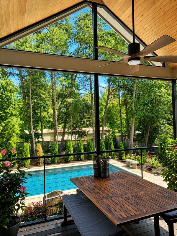 Screened patio with wooden table, ceiling fan, and pool view through large windows