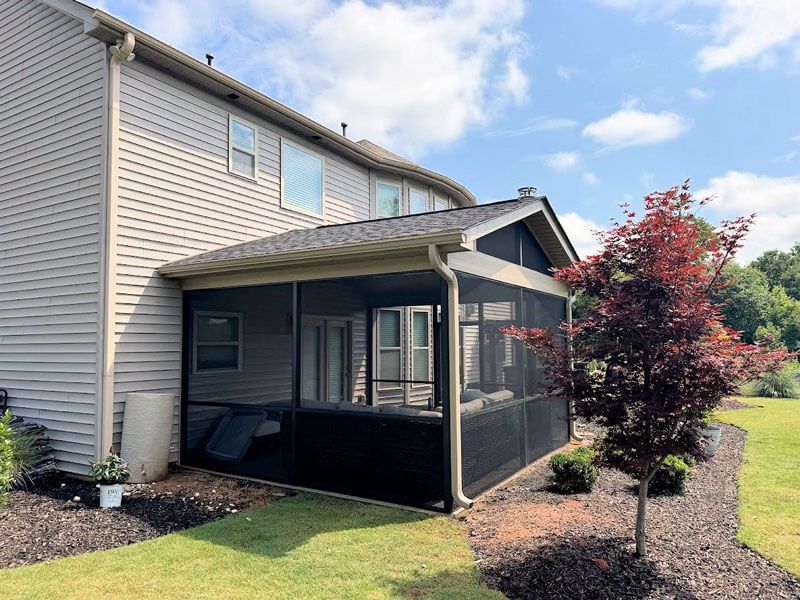 Covered screened porch attached to a beige townhouse with black mesh walls and a small patio area