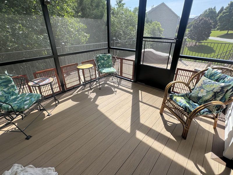 Sunlit screened porch with wicker chairs, colorful cushions, and a view of the yard