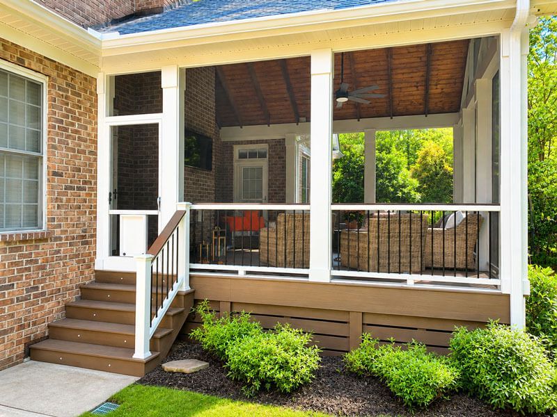 Brick house porch with white railings, wooden steps, and screened seating area under a covered roof