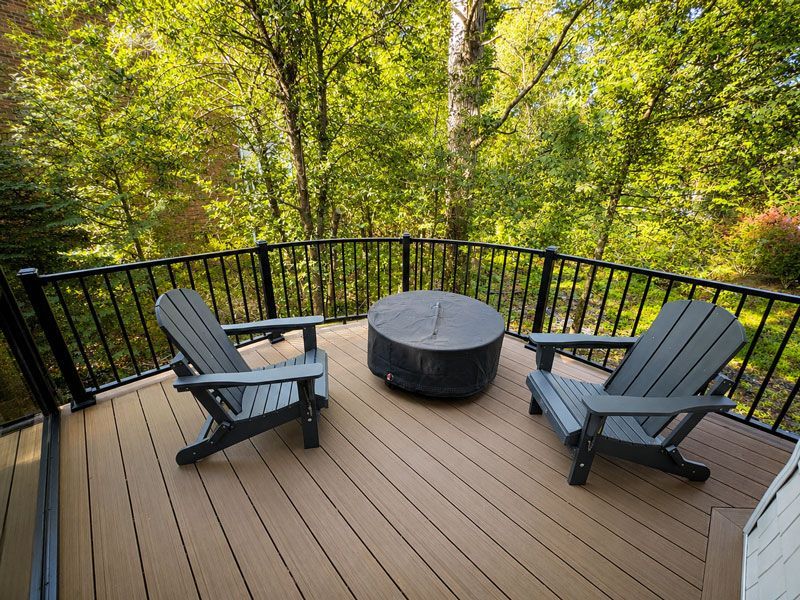 Outdoor deck with two Adirondack chairs and a round fire pit overlooking a forested area