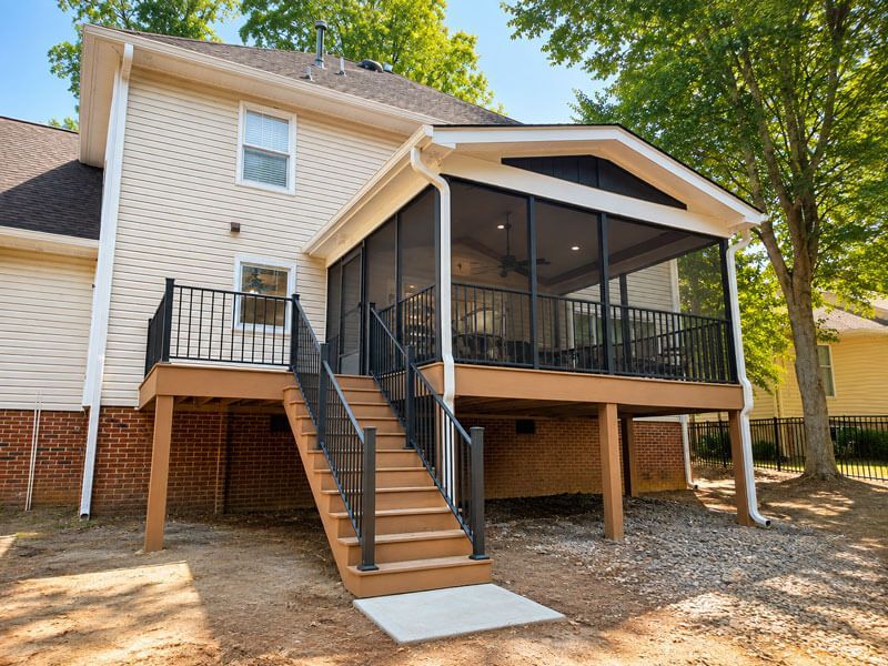 House with raised screened porch and stairs, viewed from the backyard under trees