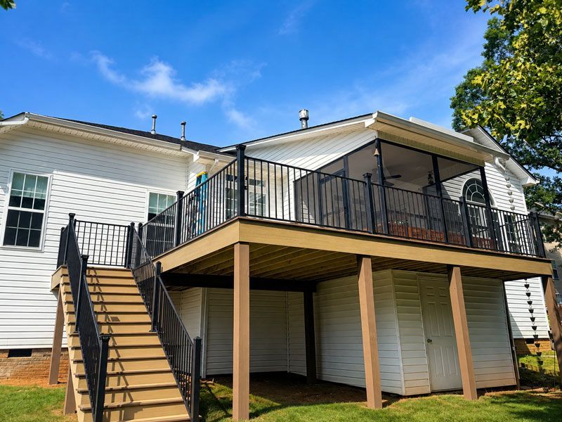 Raised wooden deck with black railings and stairs attached to a white house under a blue sky