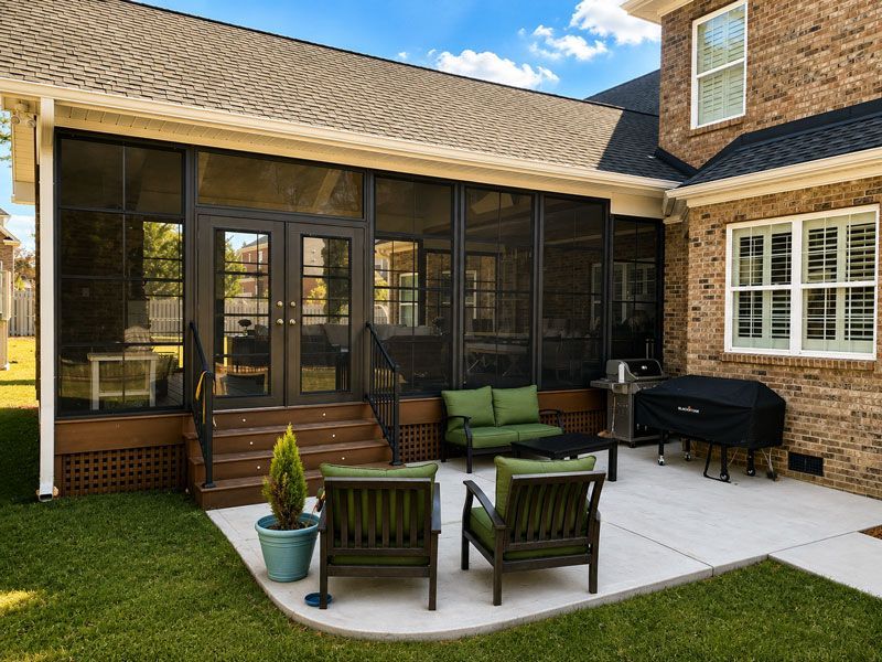 Screened patio with wicker chairs, a table, and a grill beside a brick house