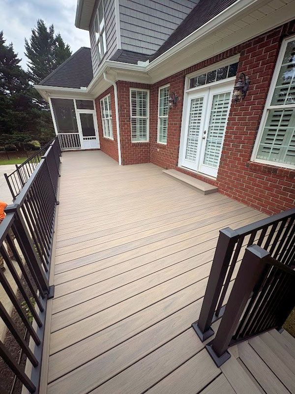 Brick house back deck with beige flooring, black railing, and white French doors.