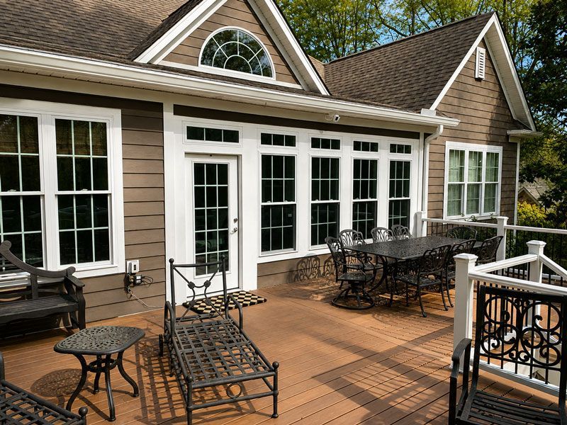 Spacious deck with black metal furniture outside a tan house with white French doors and large windows