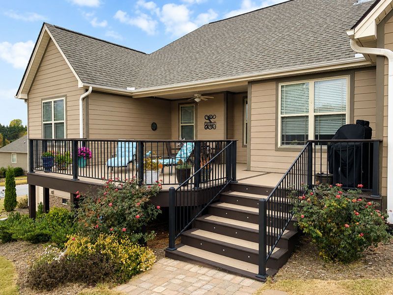 porch with black railings, steps, and outdoor seating, surrounded by shrubs.