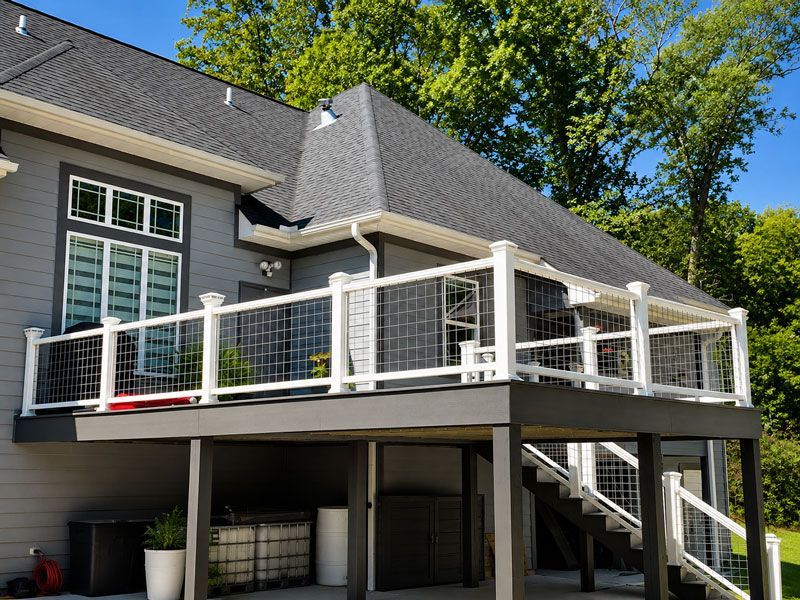 Raised deck with white railing on a gray house, showing stairs and outdoor seating area