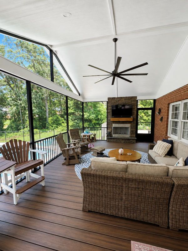 Covered outdoor patio with wicker seating, ceiling fan, fireplace, and wooded view