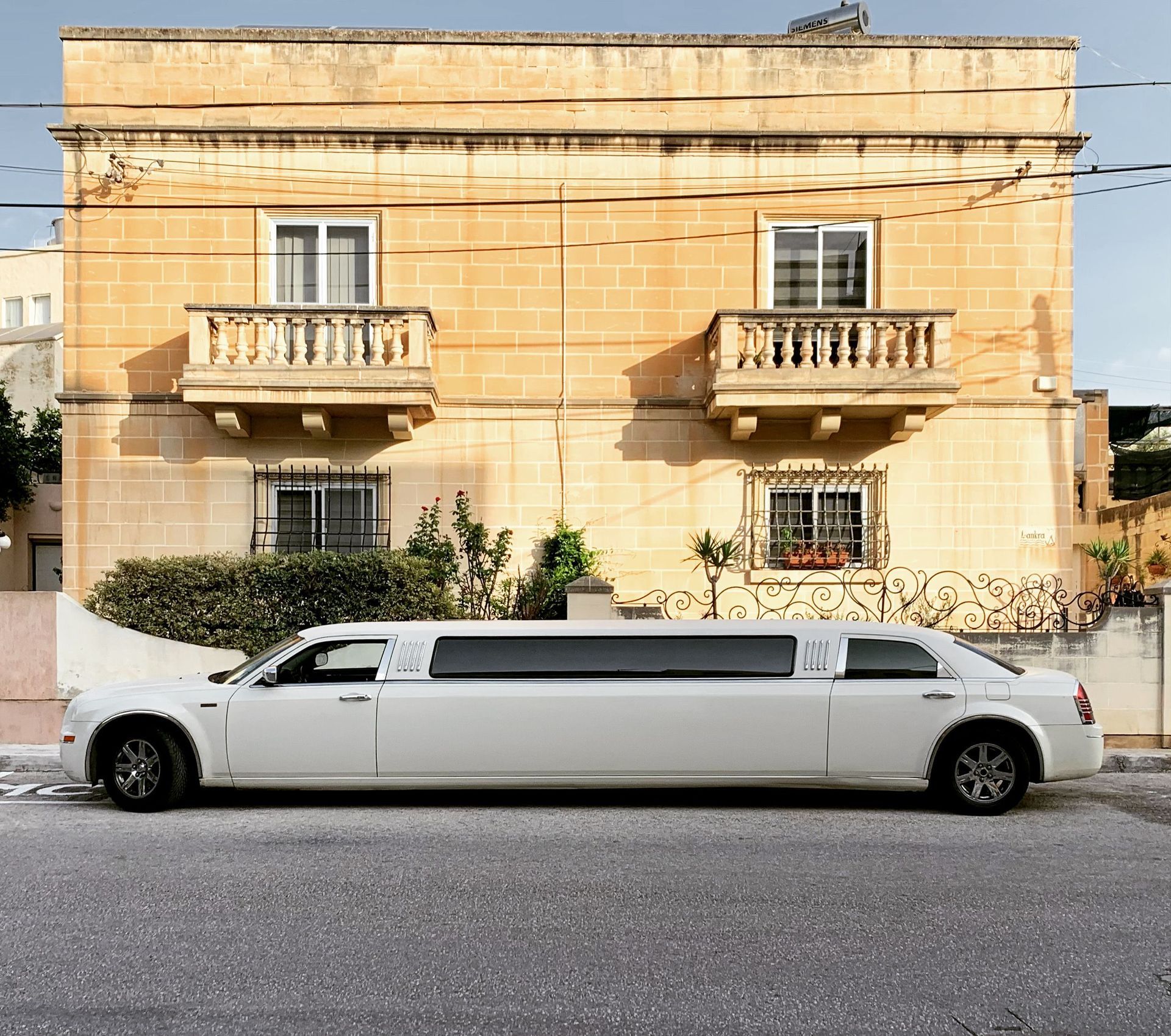 Long white limousine parked in front of a tan building with balconies and windows