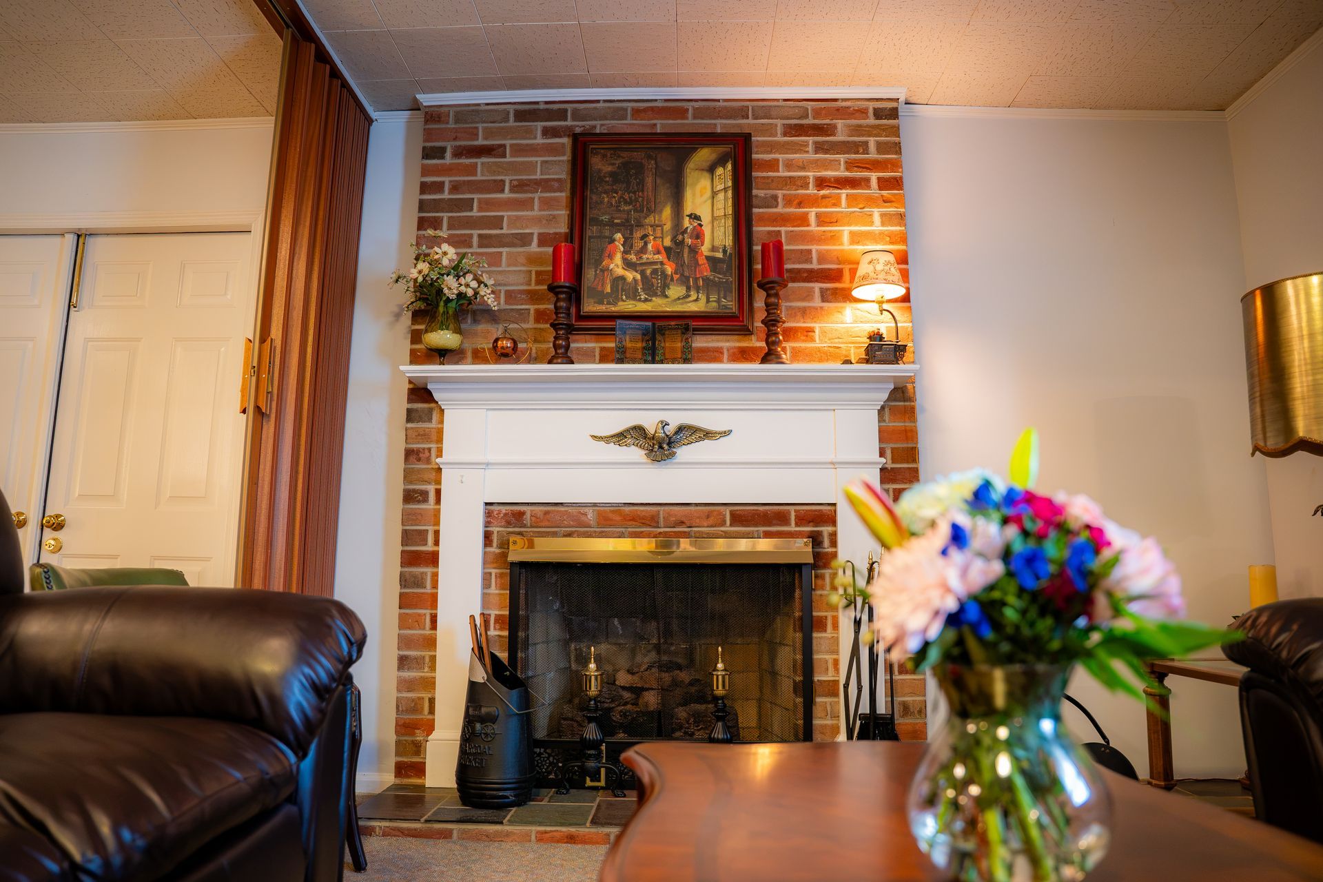 Living room with brick fireplace, mantel art, leather chair, and flowers on a table