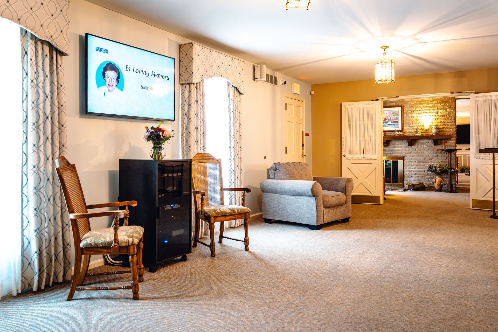 Spacious living room with chair, sofa, wall TV, and open kitchen area in warm neutral tones