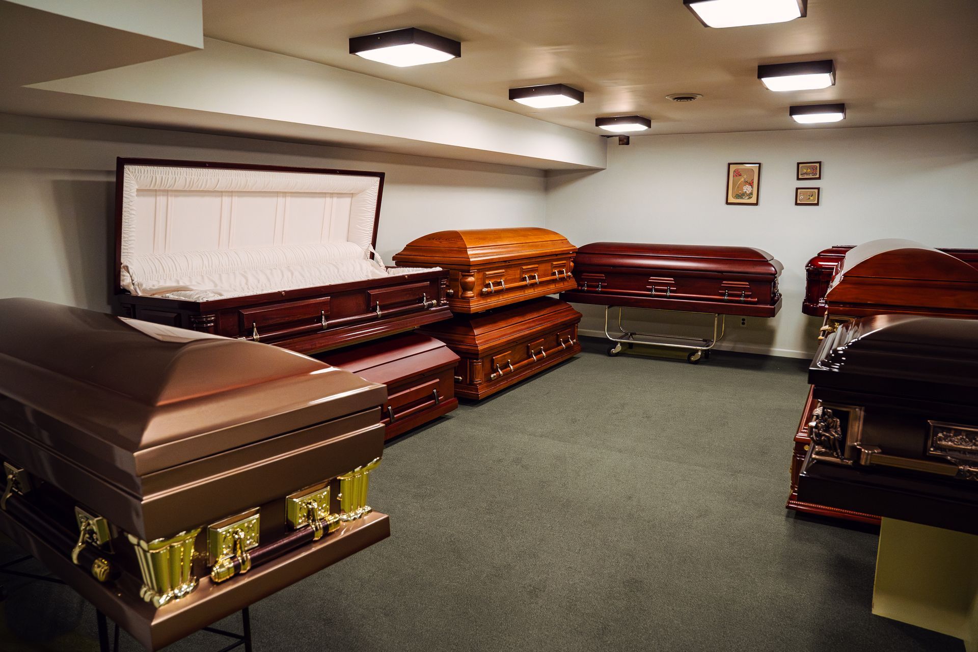 Funeral home showroom with several polished wooden coffins on display under ceiling lights
