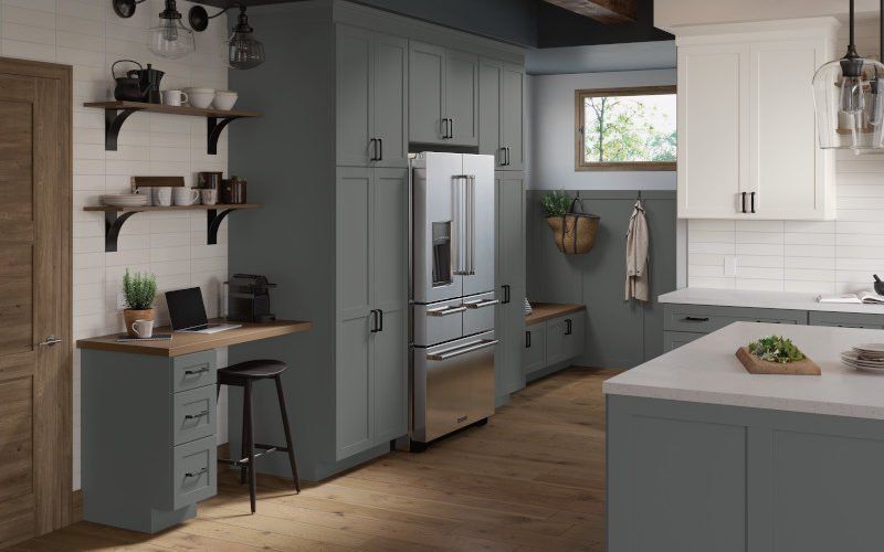 A kitchen with gray cabinets , white cabinets , stainless steel appliances , a refrigerator and a desk.