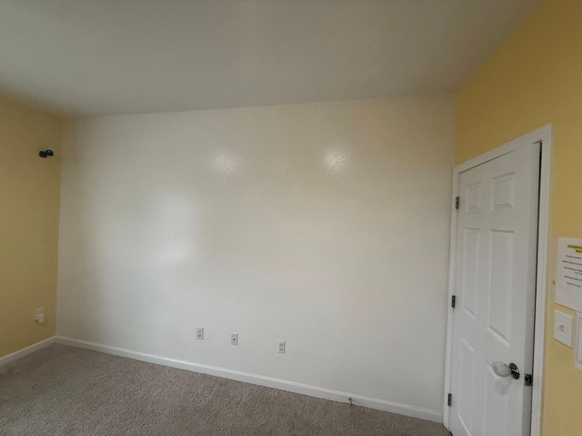 Empty beige bedroom with white walls, gray carpet, and a white door on the right.