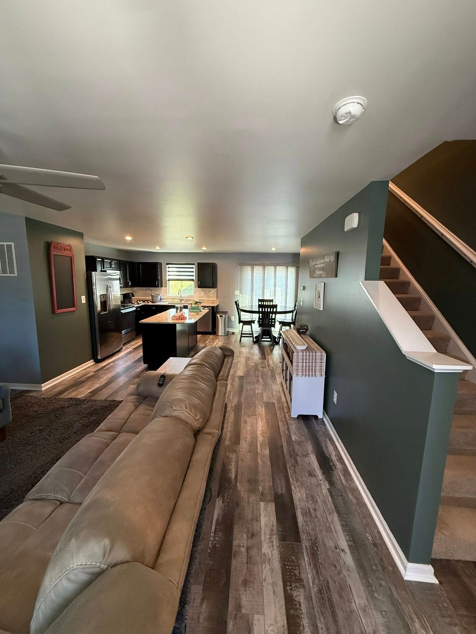 Long living room with sectional sofa, wood floors, staircase, and kitchen in the background