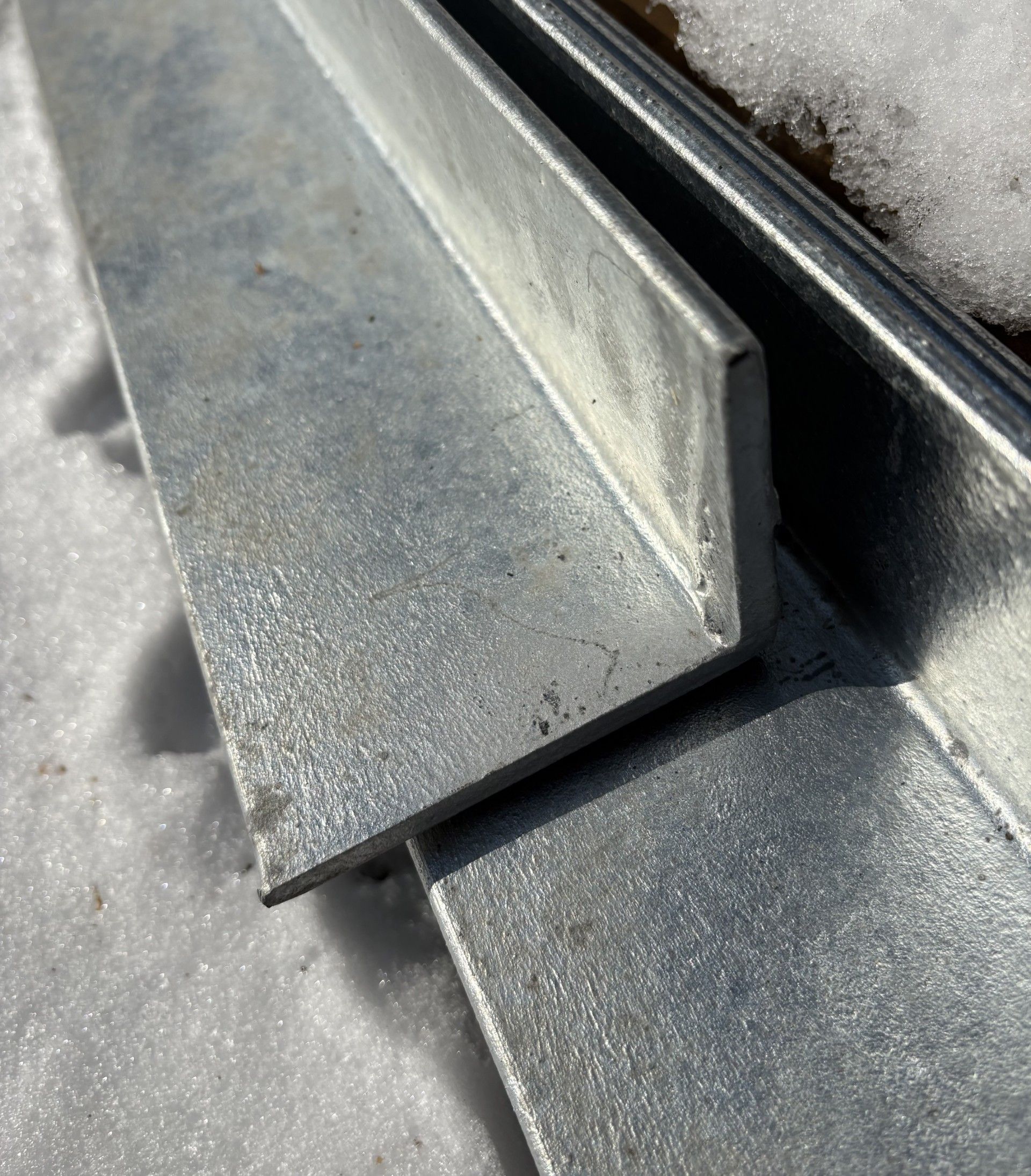 Deux équerres en acier galvanisé, à l'extérieur, sur la neige.