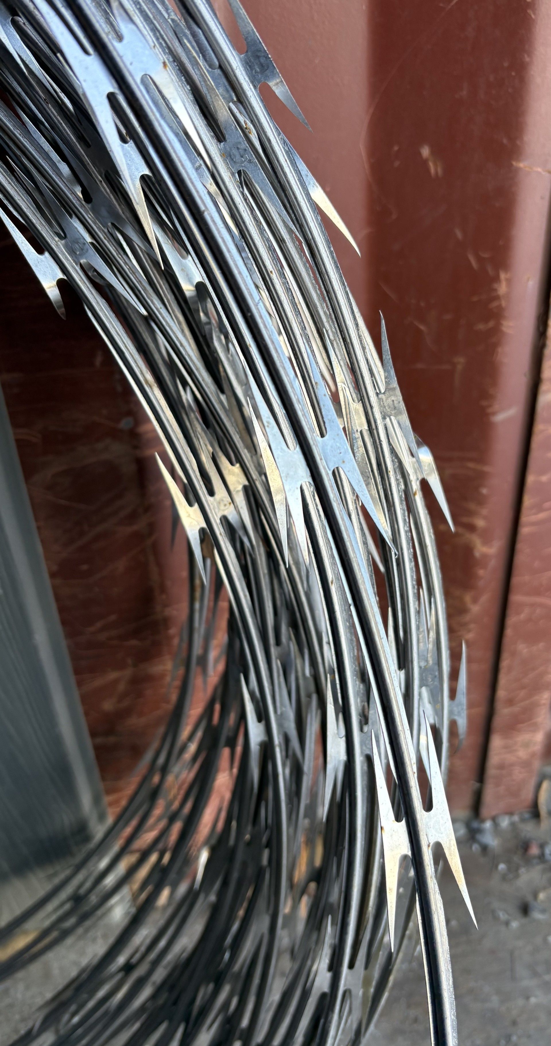 Fil de fer barbelé enroulé, métal brillant aux lames acérées, sur fond brun et gris.