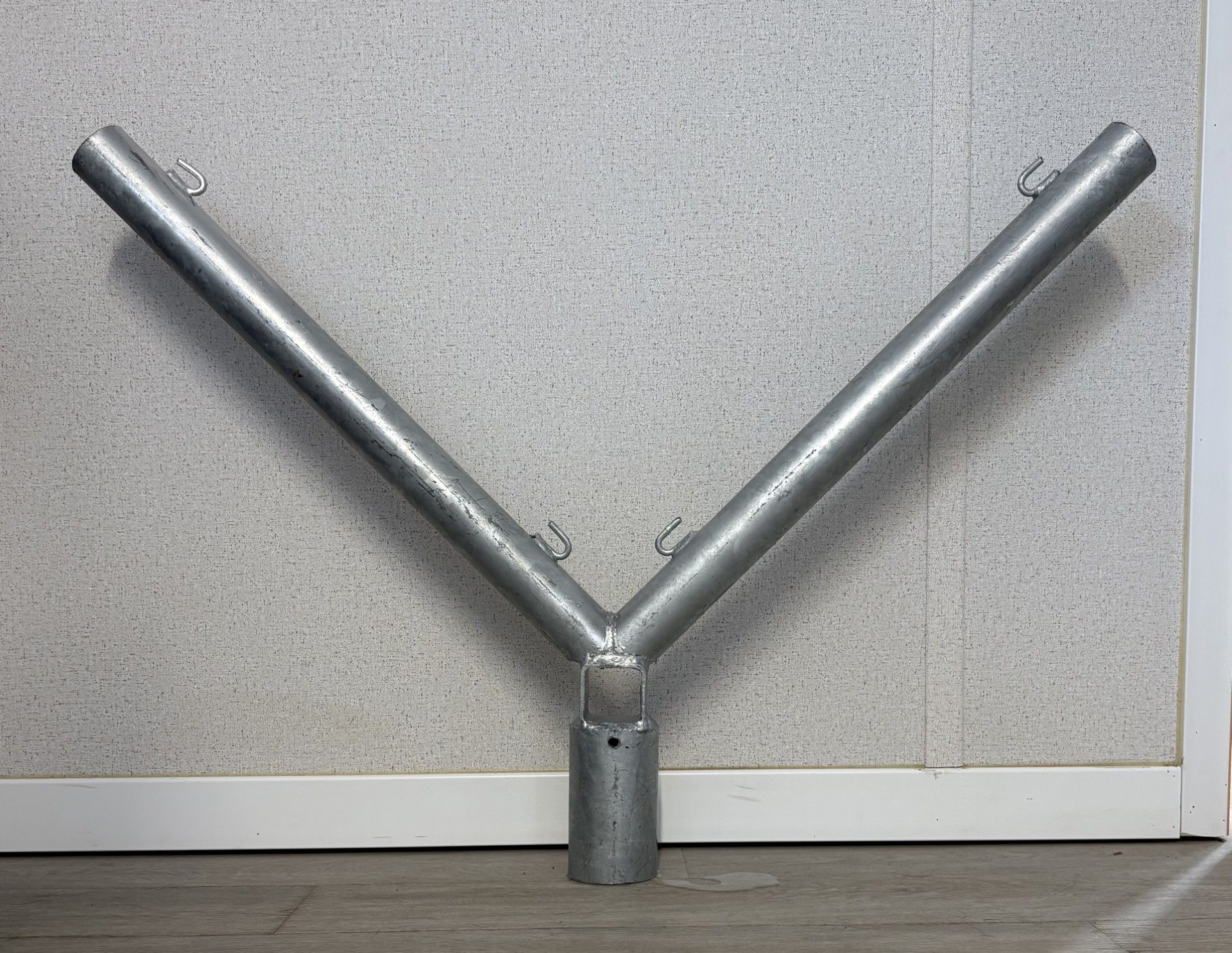 Support en métal argenté en forme de Y, avec un tube inférieur vertical et des tubes supérieurs inclinés, contre un mur texturé.