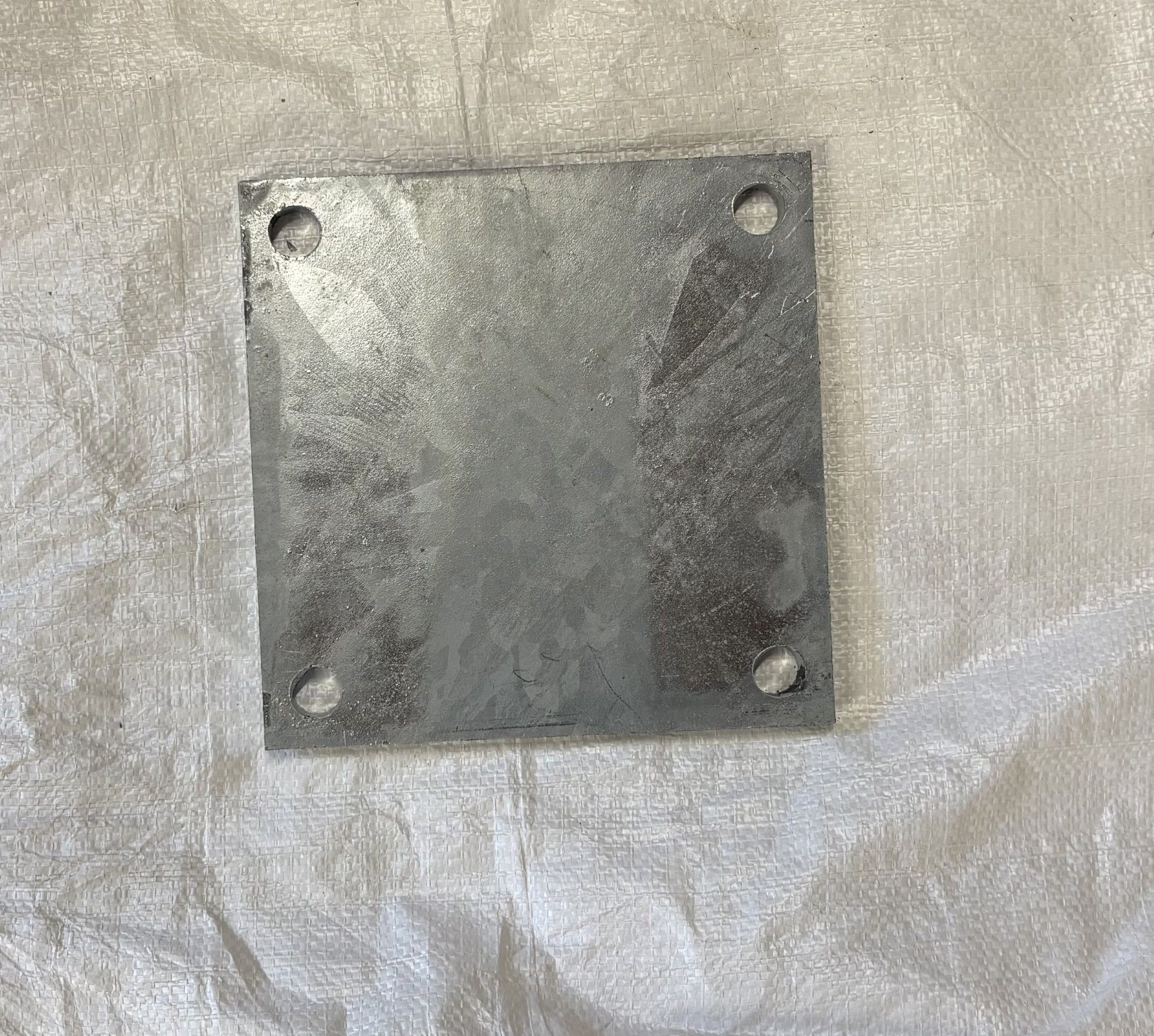 Plaque carrée en métal galvanisé avec quatre trous régulièrement espacés.
