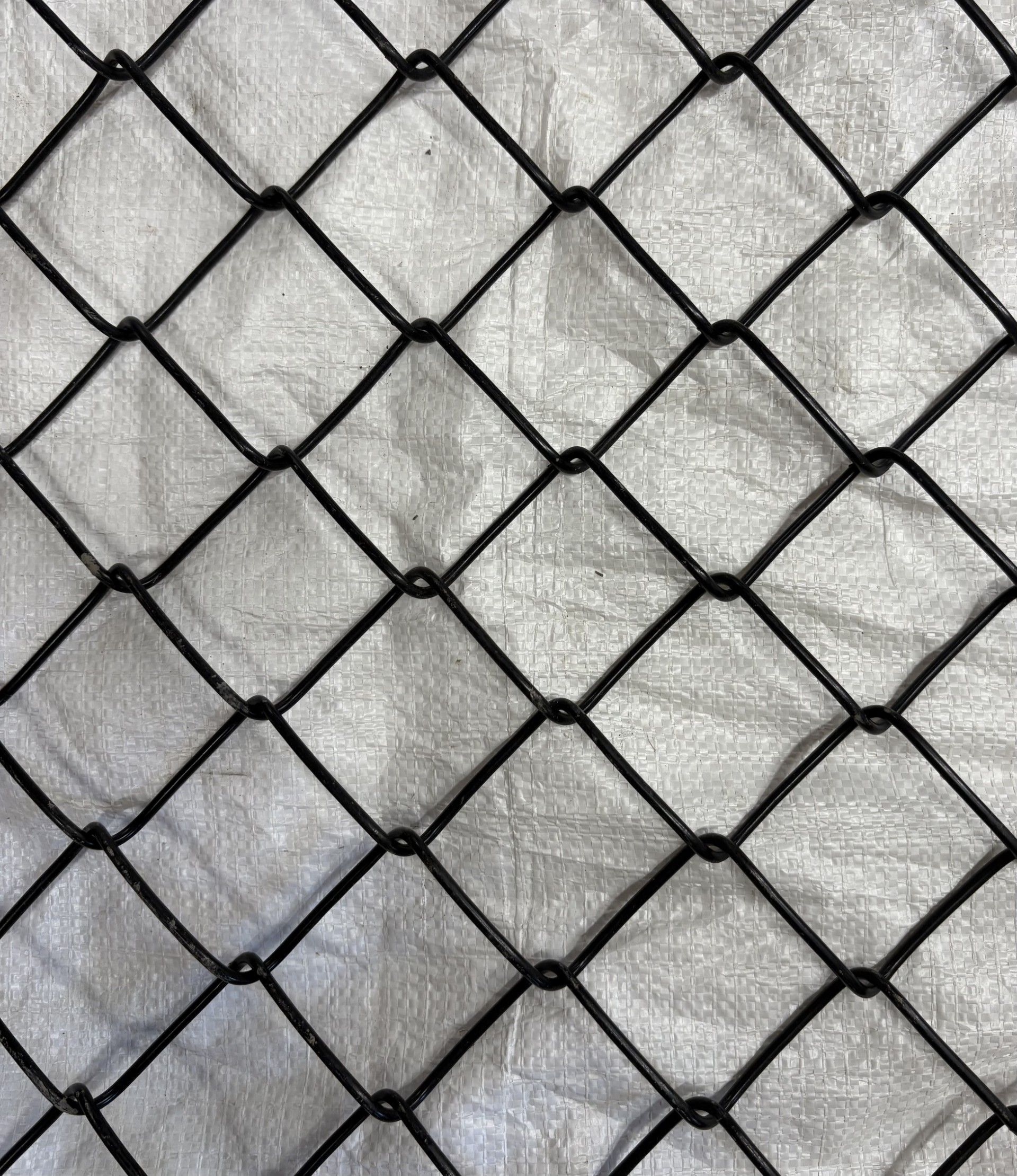 Motif de clôture en grillage noir sur fond gris clair texturé.
