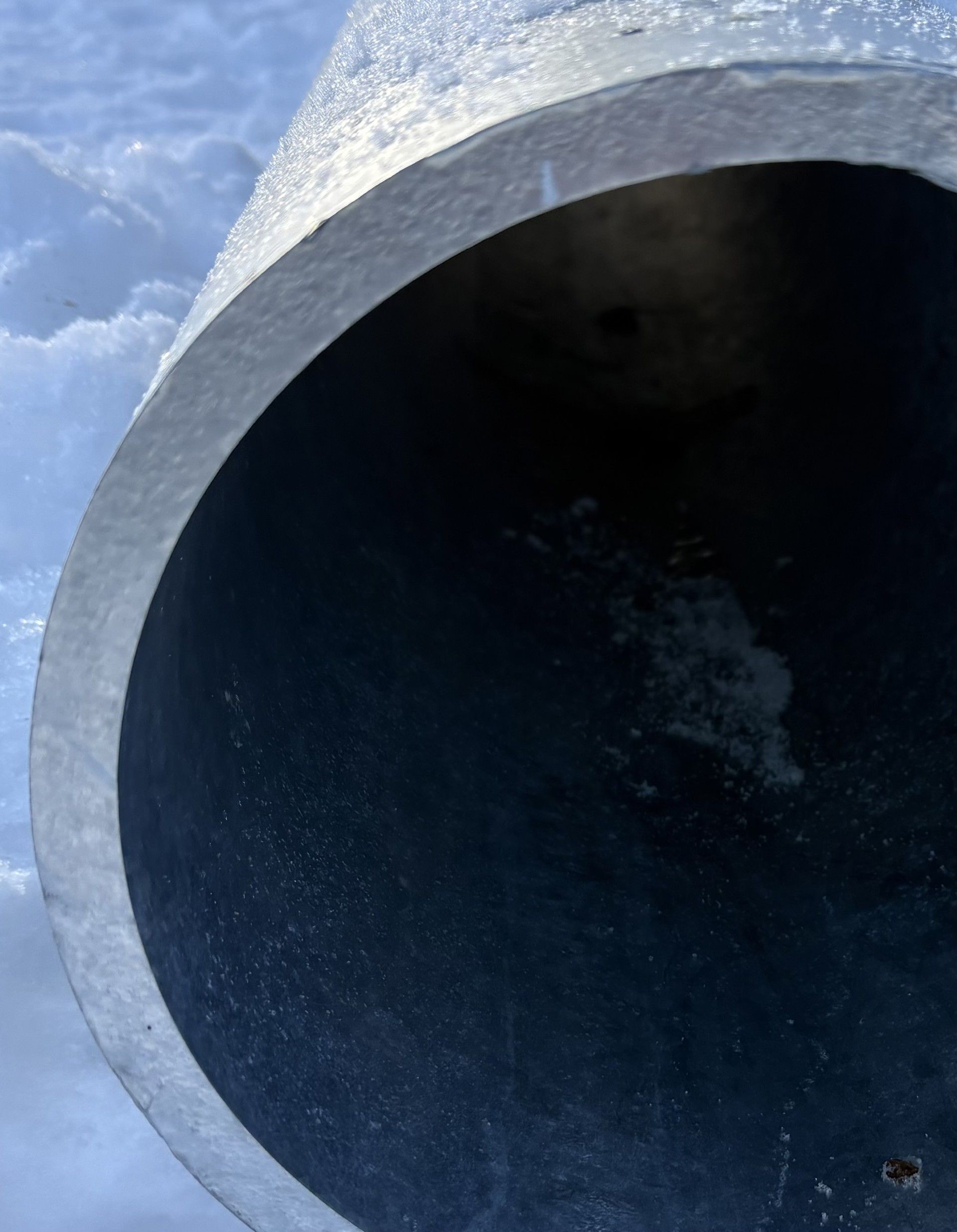 À l'intérieur d'un grand tuyau métallique sombre, incliné vers le haut, enfoui dans la neige.