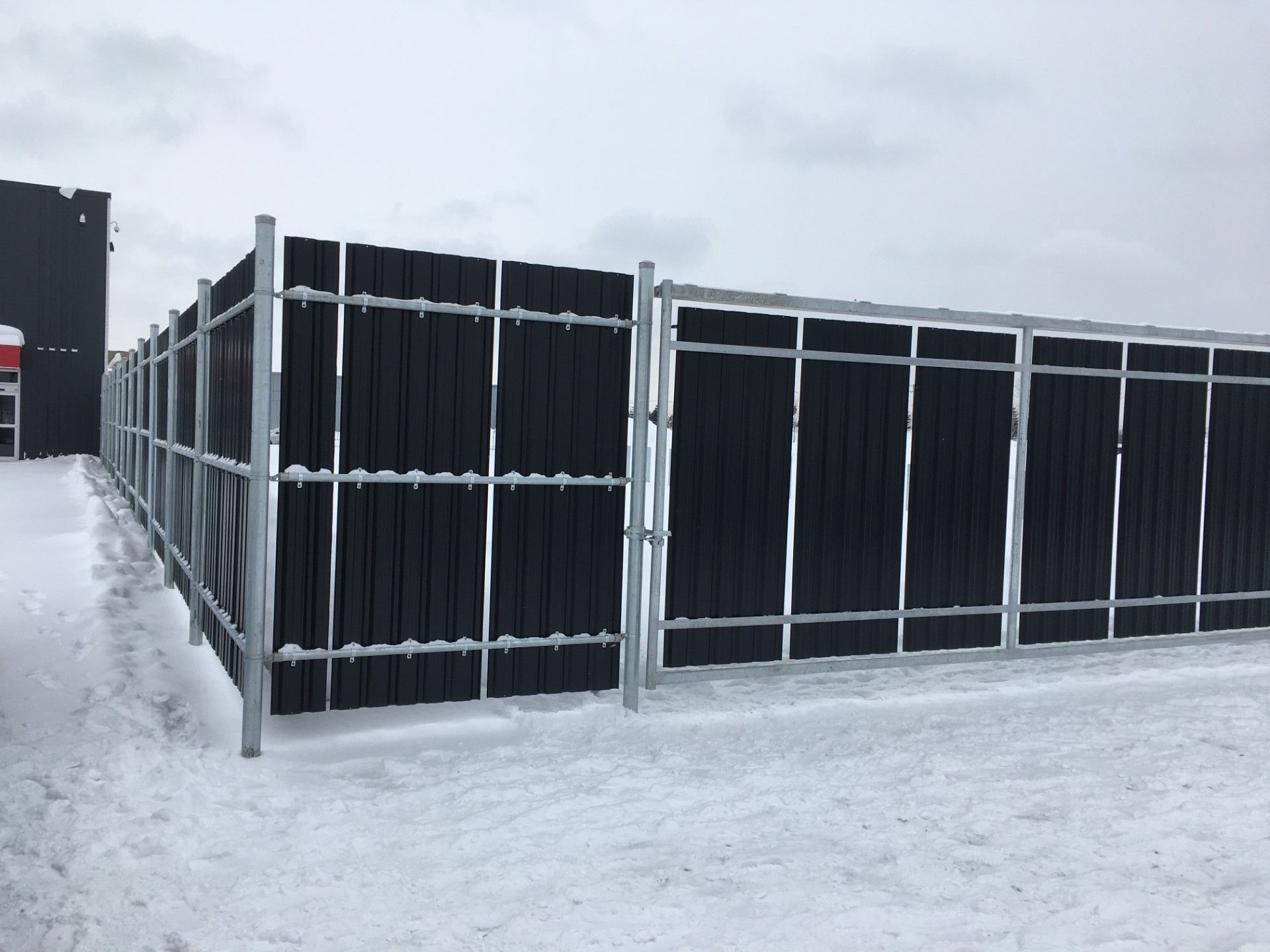 Black wooden fence with a metal frame in a snowy area.