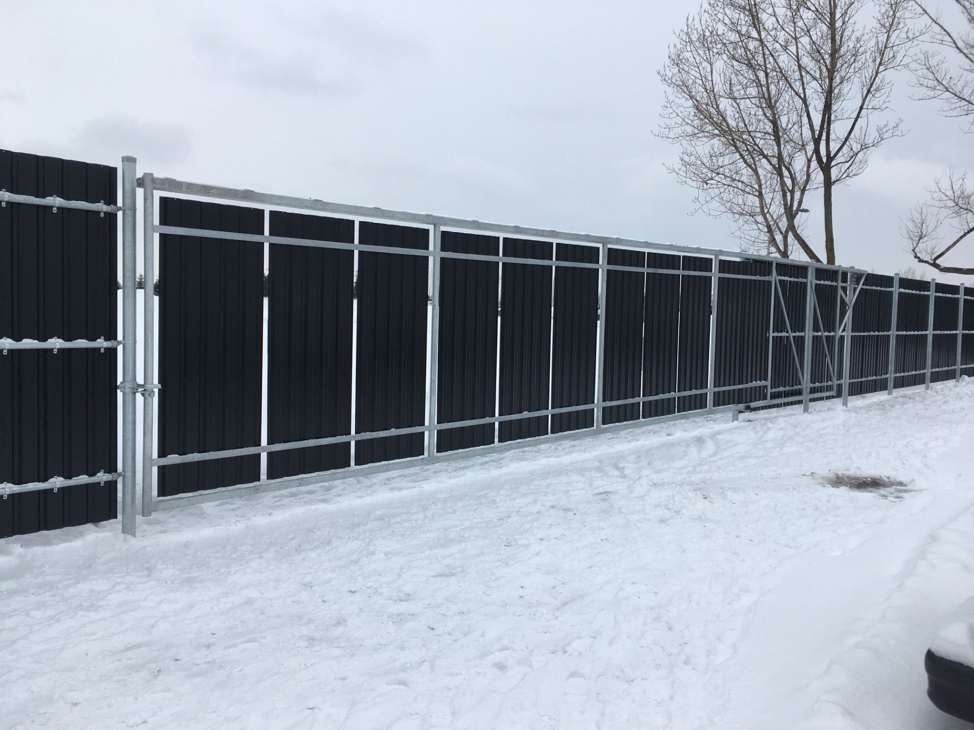 Black fence with metal frame, covered in snow, in a snowy outdoor setting.
