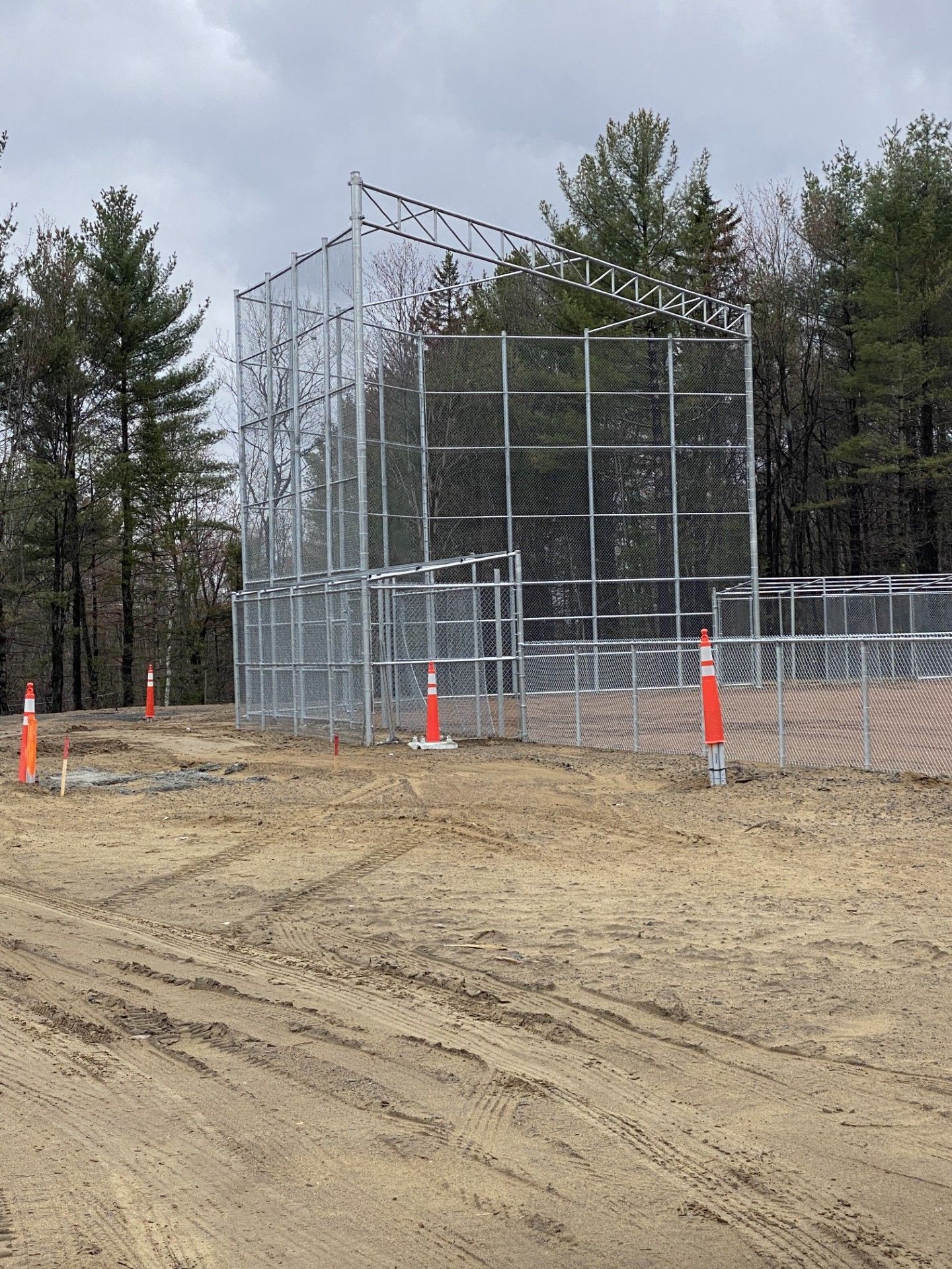 A tall, multi-level chain-link structure in a dirt lot, with orange traffic cones.