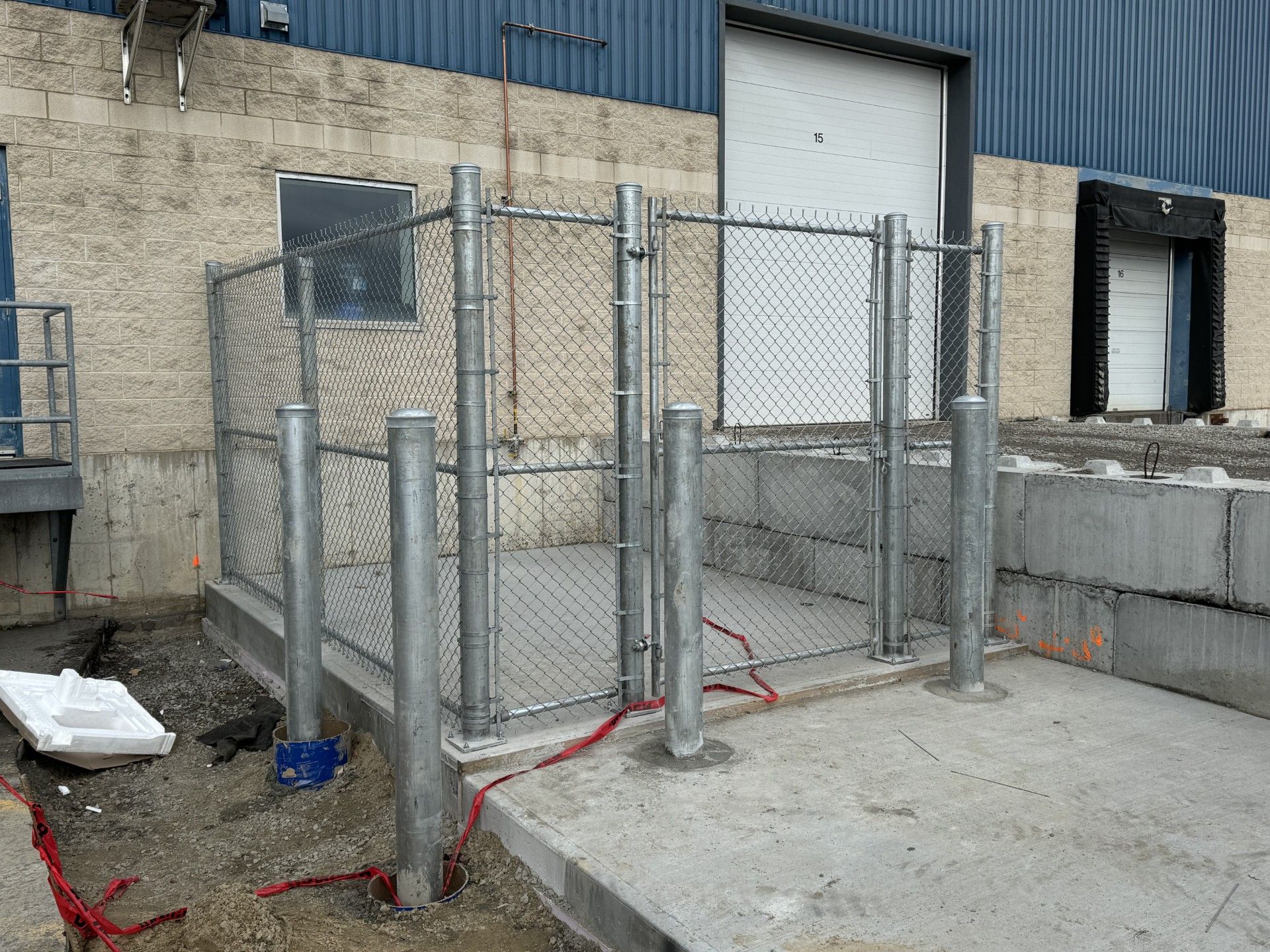 Chain link fence enclosure at a loading dock. Gray concrete, blue building.