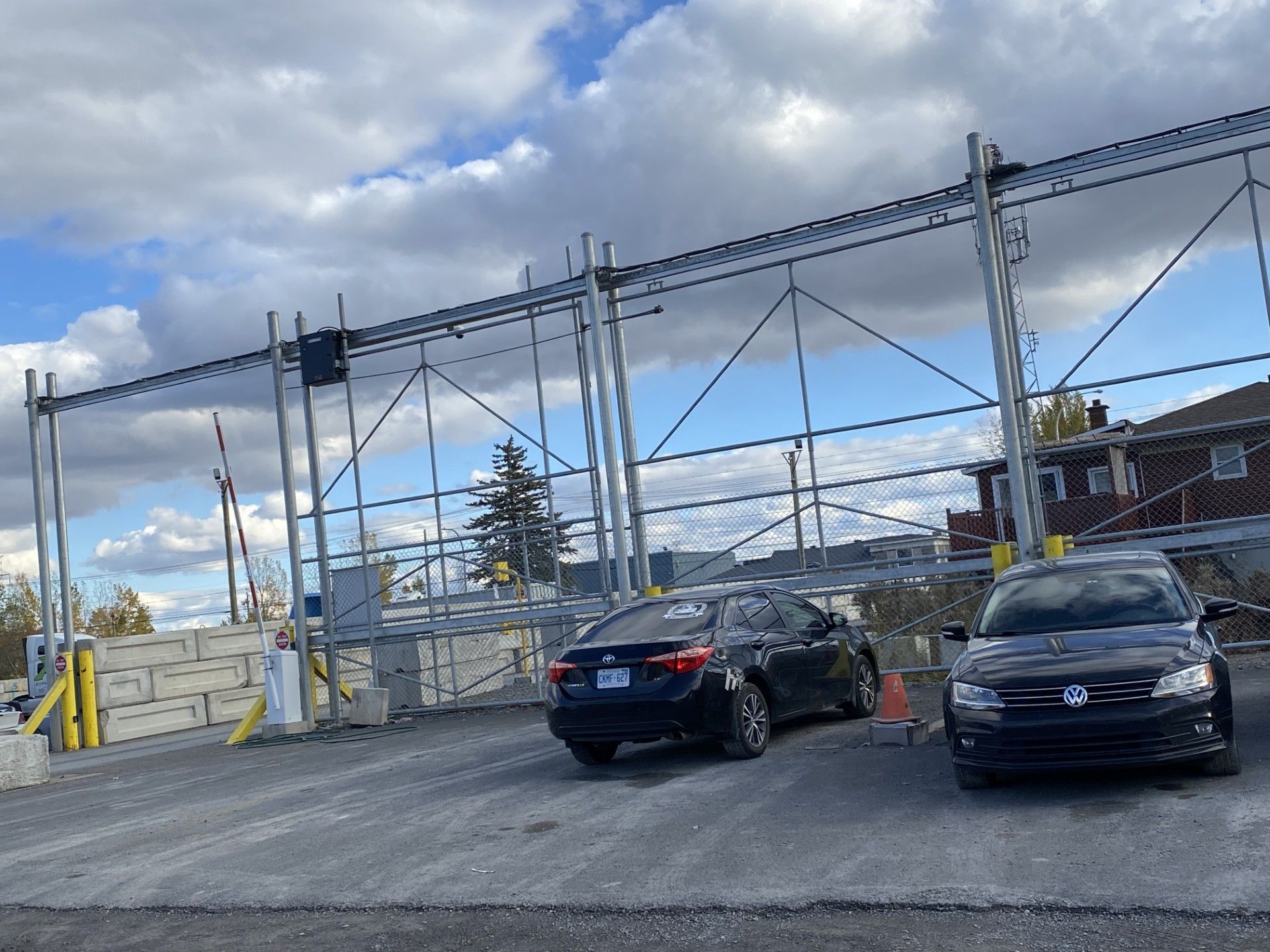 Cars driving through a security checkpoint with overhead gates, on a cloudy day.