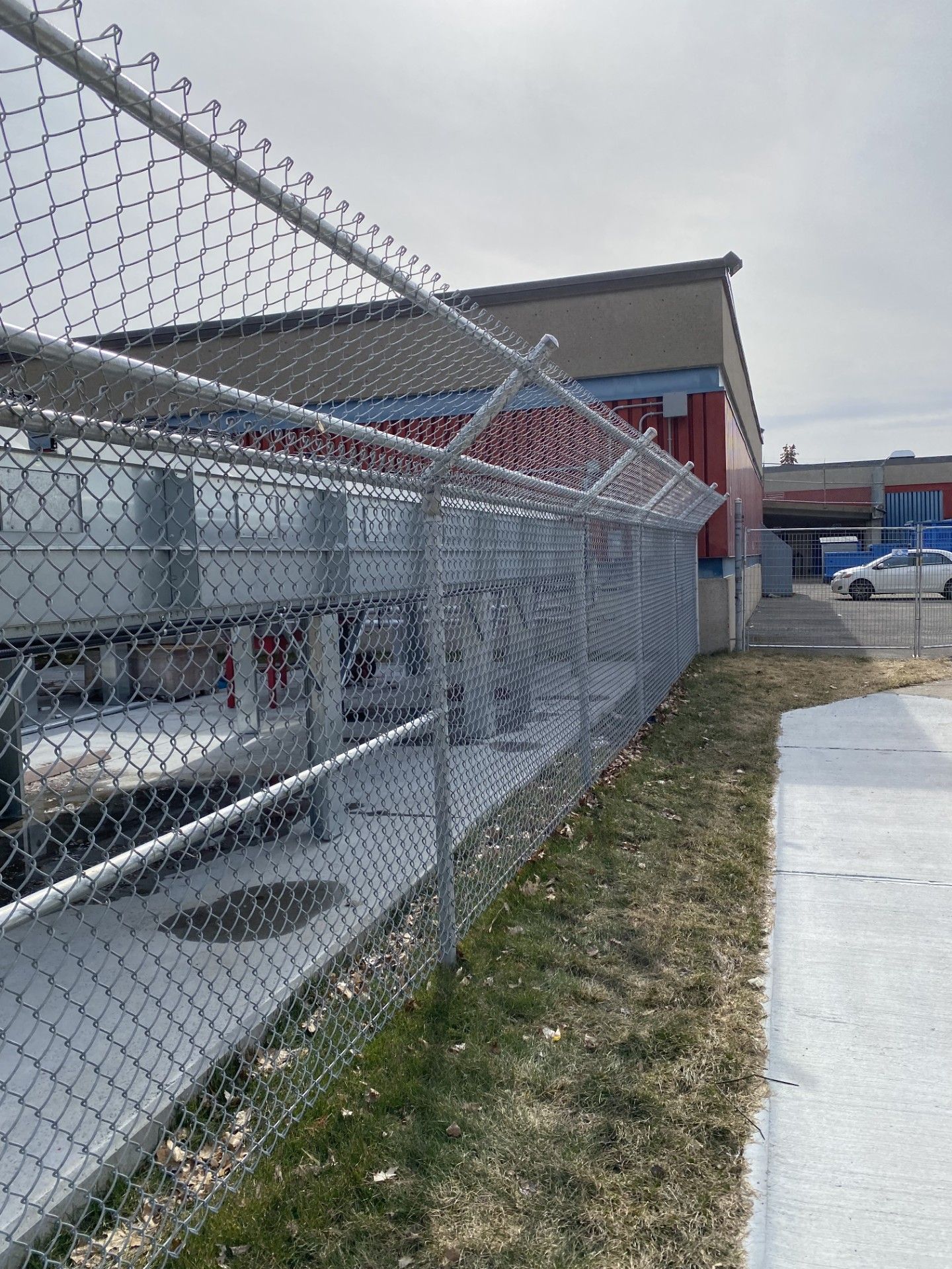 Chain-link fence with barbed wire around a building, on a partly cloudy day.