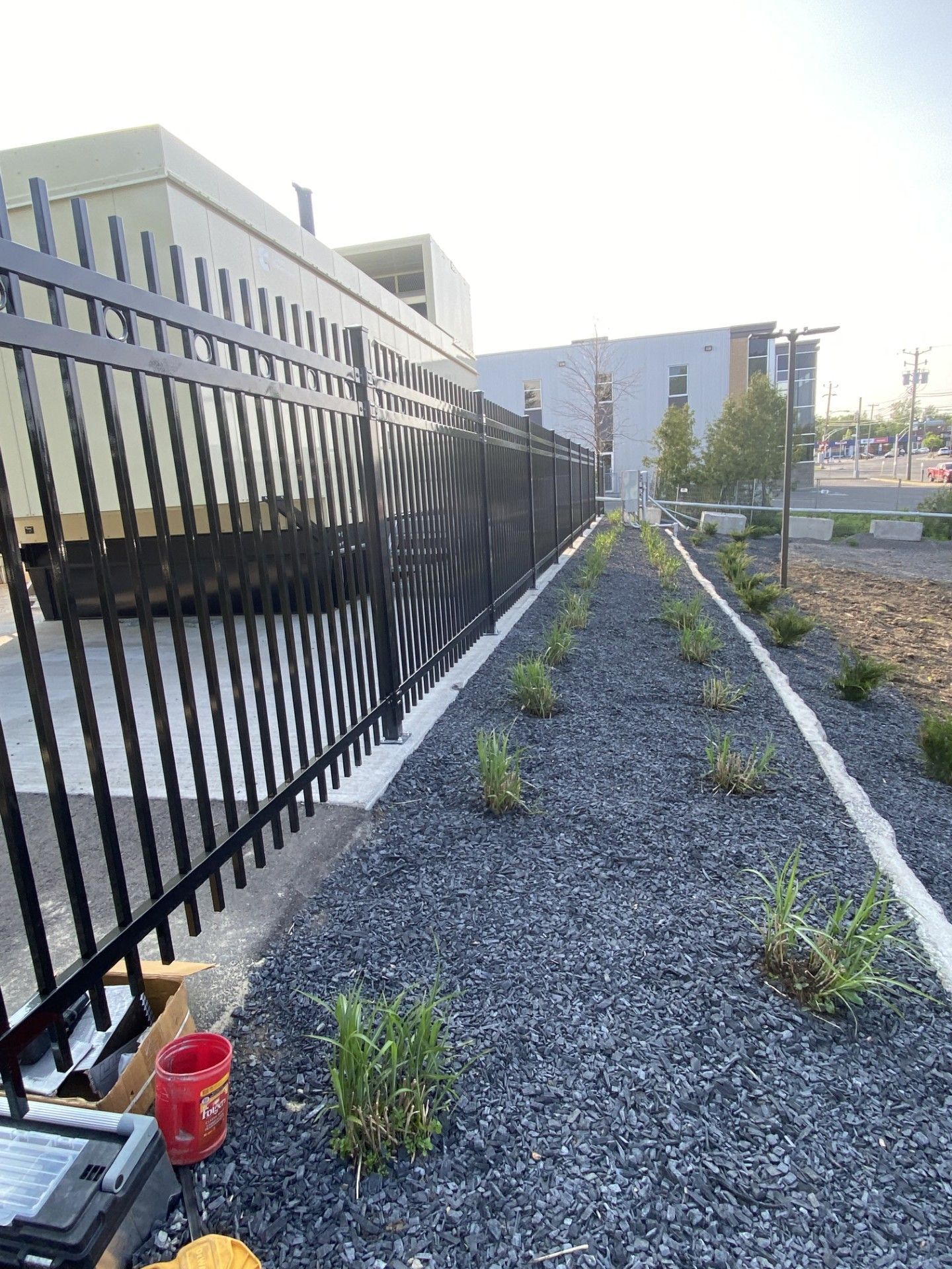 Black metal fence with a decorative section, next to a landscaped strip of black gravel and plants.