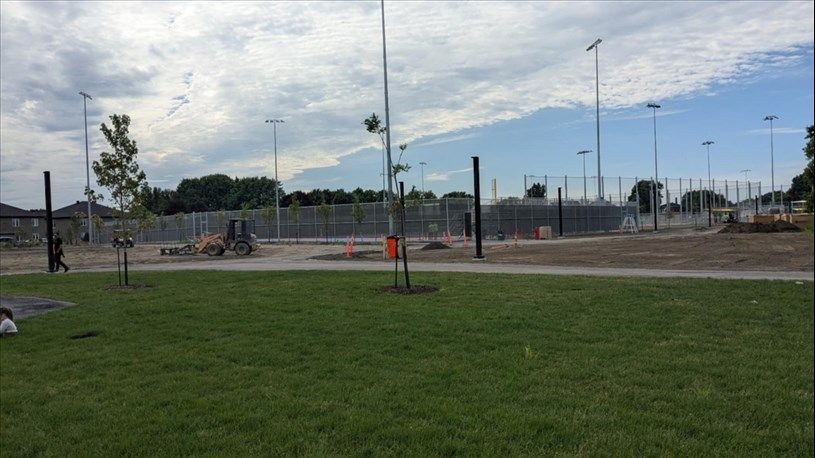 Grassy park with new fencing and construction; sky with clouds.