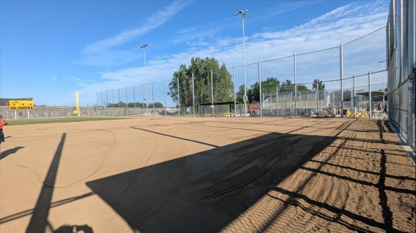 Empty baseball field under a blue sky, with a tall fence and stadium lighting.